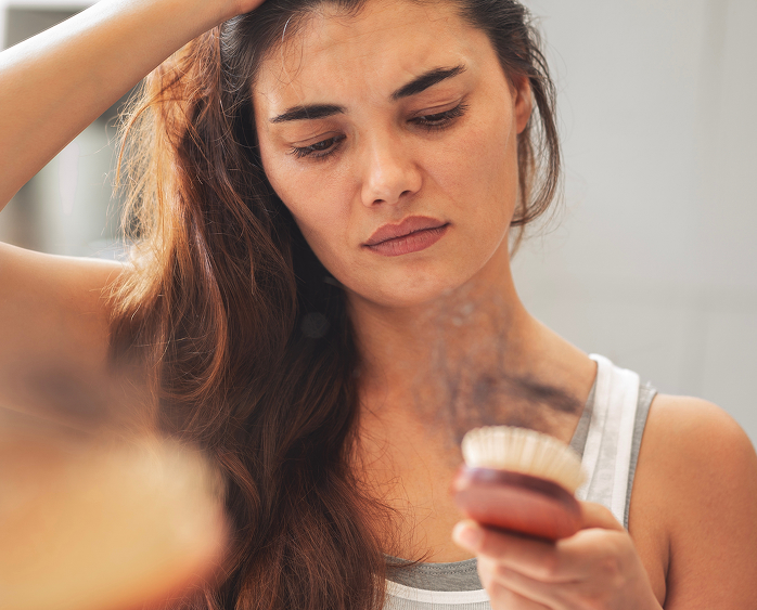 Woman examining hair loss in a brush, illustrating shedding that may occur after a GLP-1 dose increase.